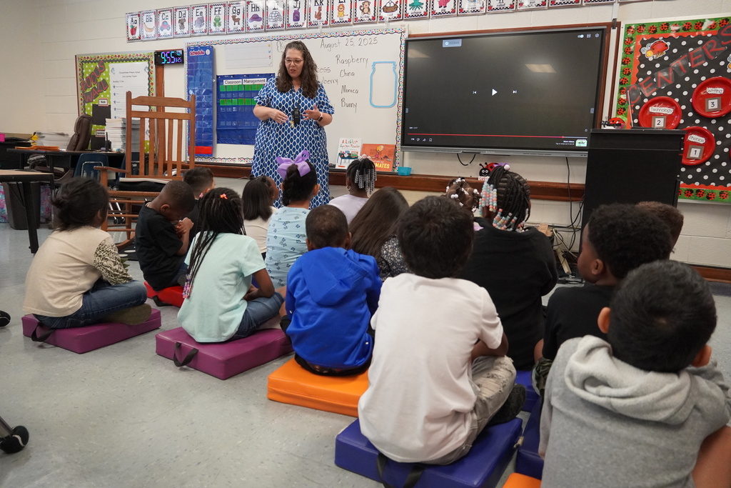 Teacher addresses young students seated on mats during class circle time.