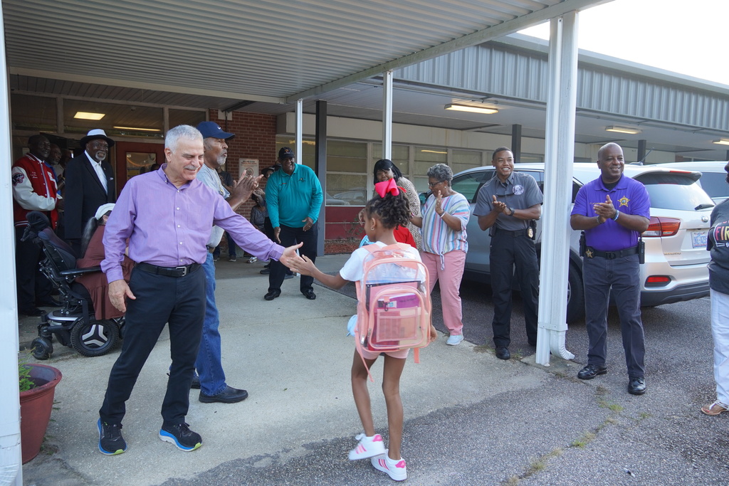 Student with pink backpack greeted by community members outside school on the first day.