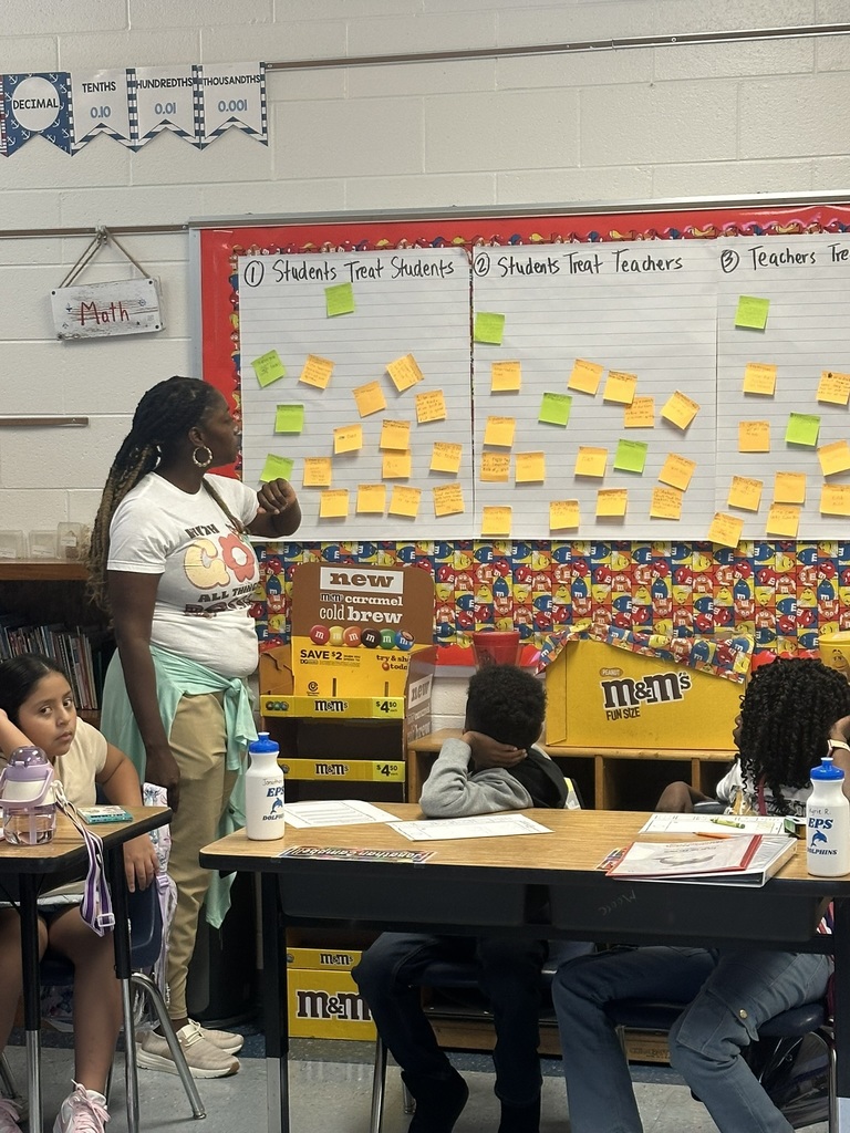 A teacher stands beside a chart filled with sticky notes as students discuss how to treat one another and their teachers.