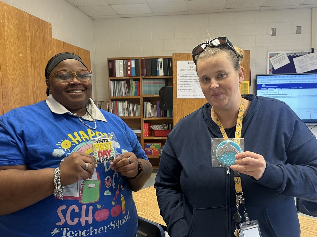 Two staff members stand together holding dolphin and first day cookies.