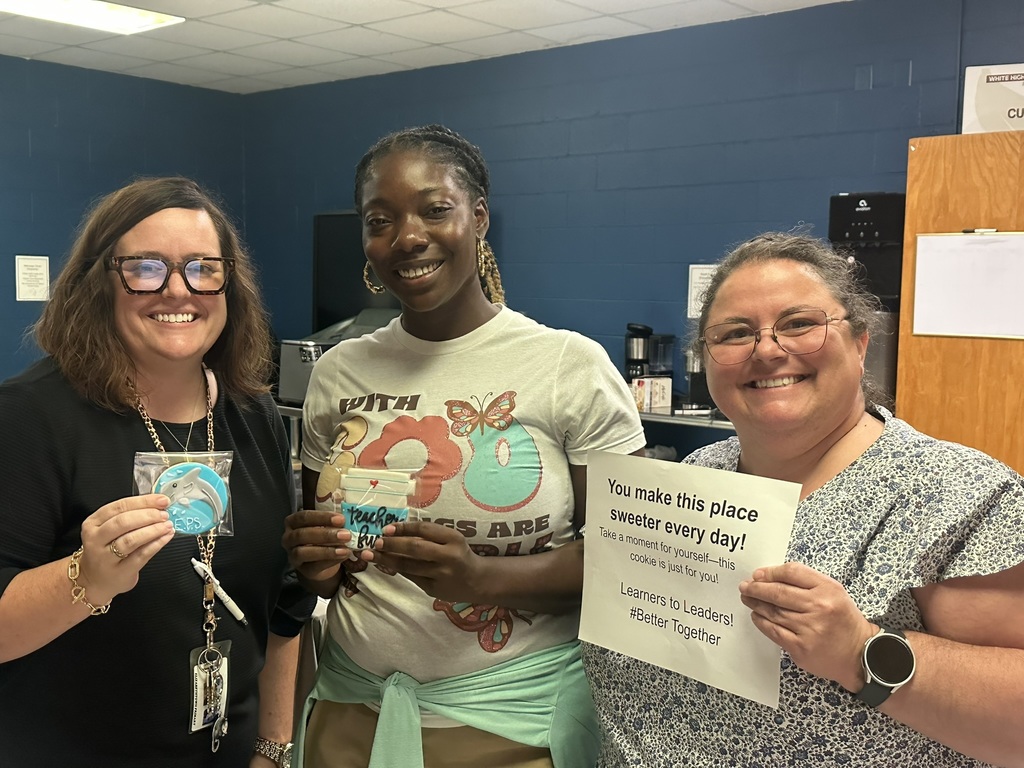 Three staff members stand together holding cookies and the appreciation sign, smiling for the camera.