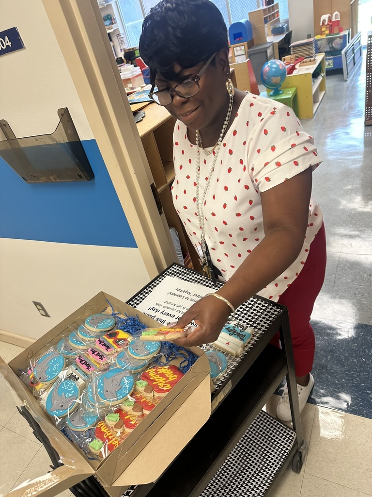 teacher smiles while holding a “Teacher Fuel” cookie shaped like a coffee cup.