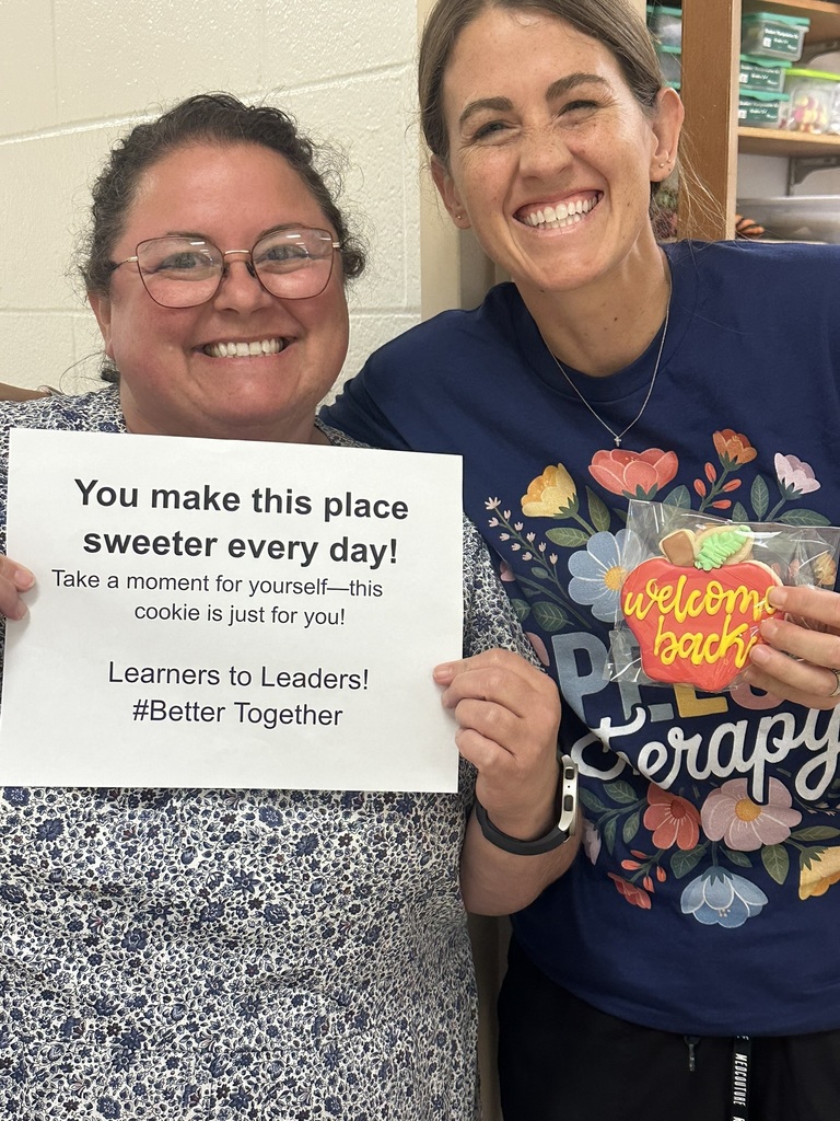 Two smiling staff members hold a cookie and sign that says, “You make this place sweeter every day!”