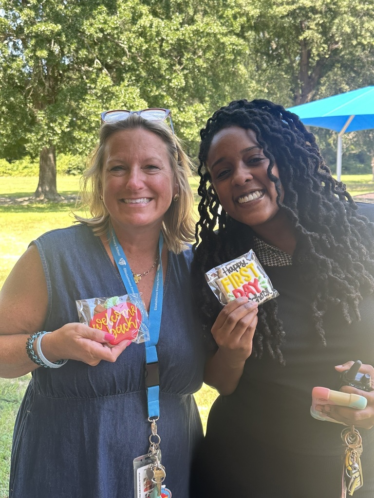 Two staff members outdoors hold welcome and first day cookies, smiling in the sunshine.