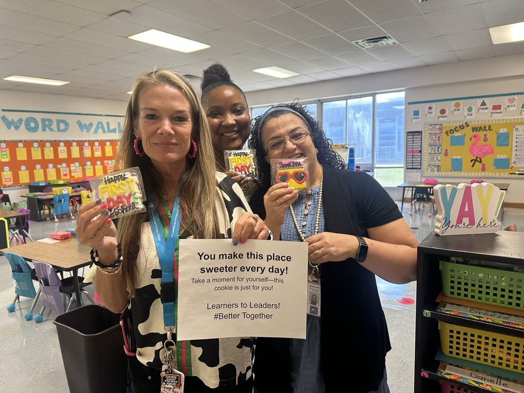 Three staff members stand together holding dolphin and first day cookies.