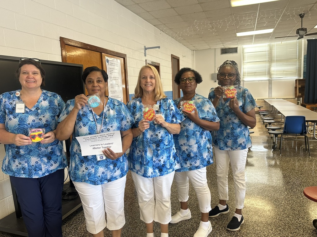 Five cafeteria staff members in matching blue uniforms hold decorated cookies and a thank-you sign.