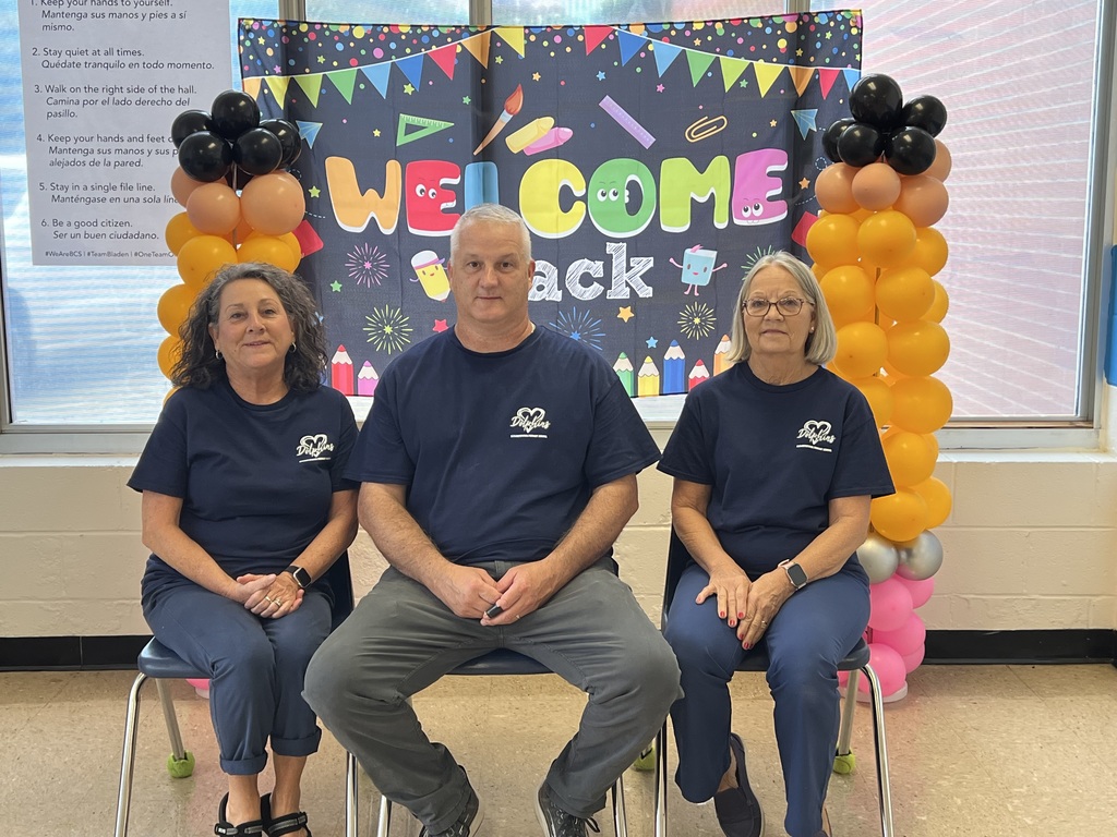 Three members of our custodian team sitting in front of back to school welcome sign.