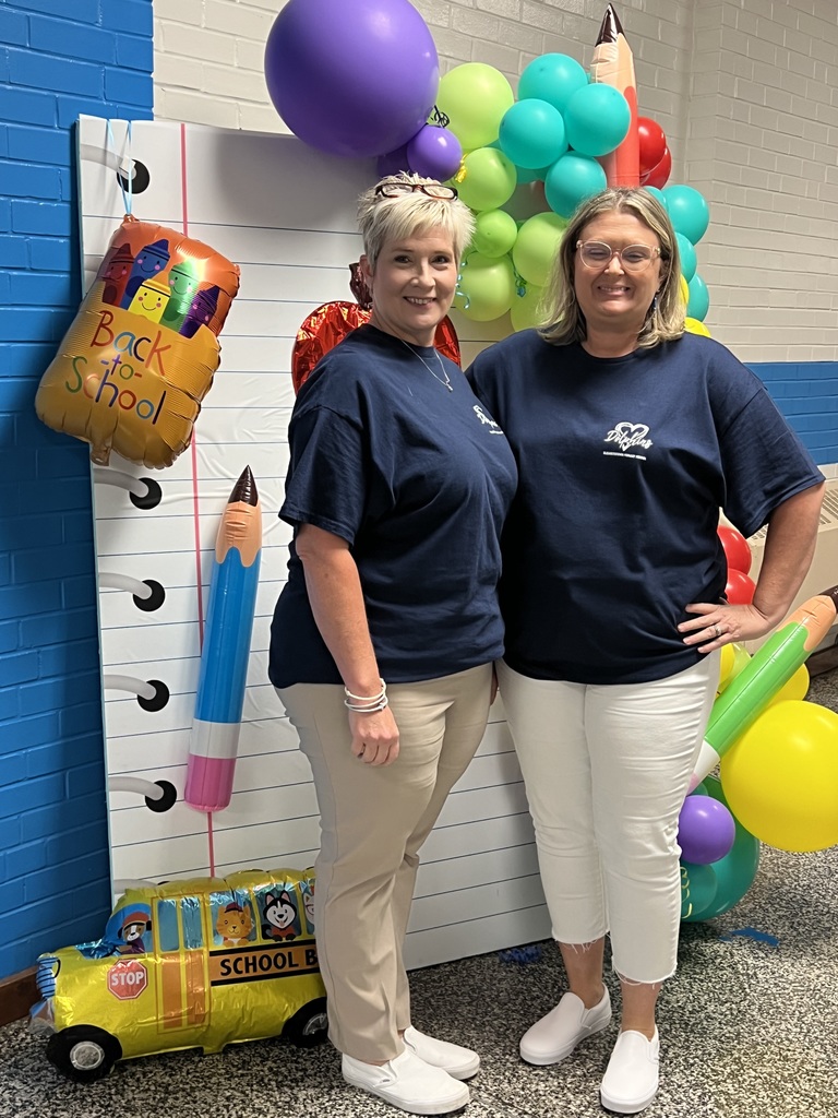 Two ladies in school tee shirts in front of back to school photo prop with balloons.