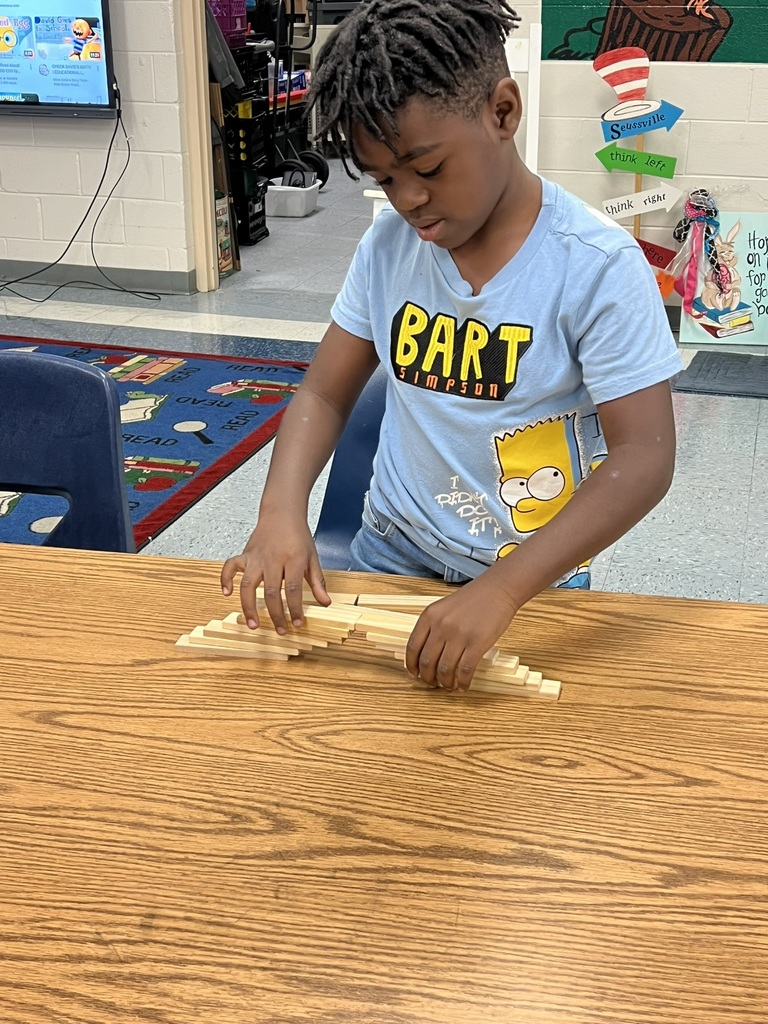 A young student carefully stacks wooden blocks on a classroom table to create a bridge. He is focused on balancing the pieces as he builds his structure.