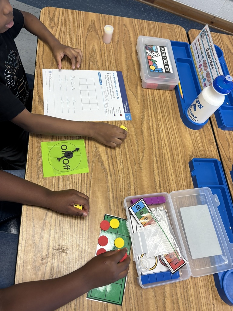 A student places red and yellow counters on a ten-frame mat while working on an addition worksheet, with a math tool kit open on the desk.