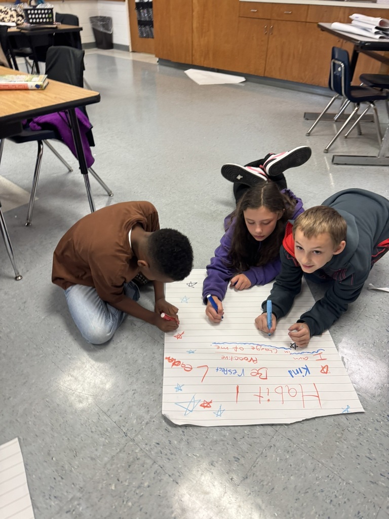 Three students work closely on the floor, adding drawings and words to their Habit 1 poster.