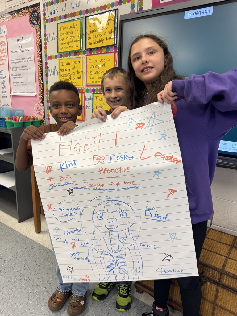 Three students stand together holding their colorful Habit 1 poster filled with writing and a large drawing.