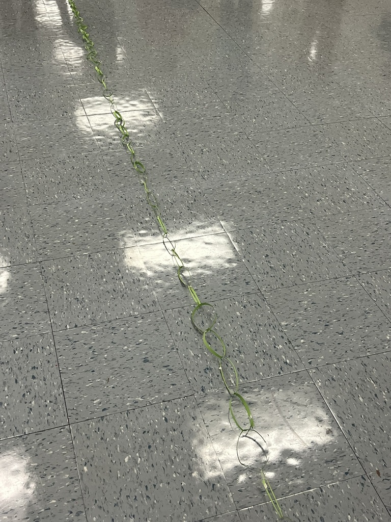 Close-up of a green paper chain laid out across the shiny tile floor, showing the neat links connected together.