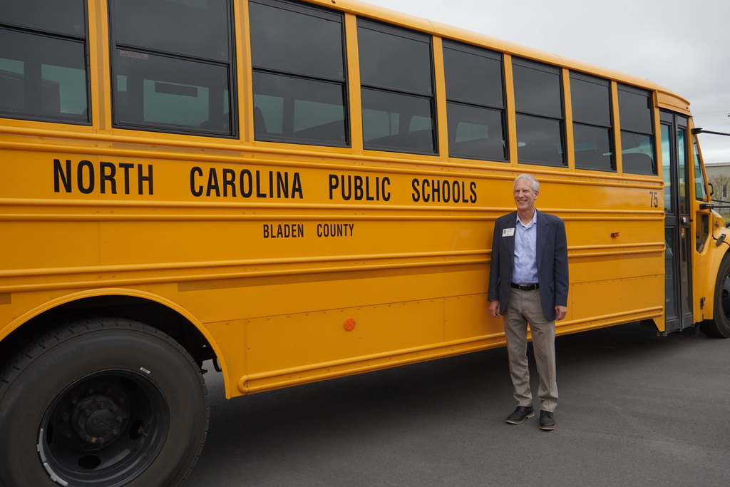 A man stands next to a bright yellow school bus labeled “North Carolina Public Schools – Bladen County.”