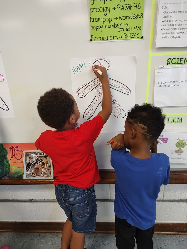 Two students work together on a figure labeled “Happy,” adding details like a big smile and cheerful body markings.