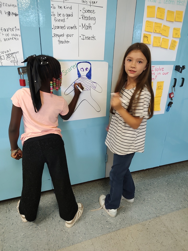 A student colors a figure labeled “Scared” with wide eyes and a striped body while another student watches.