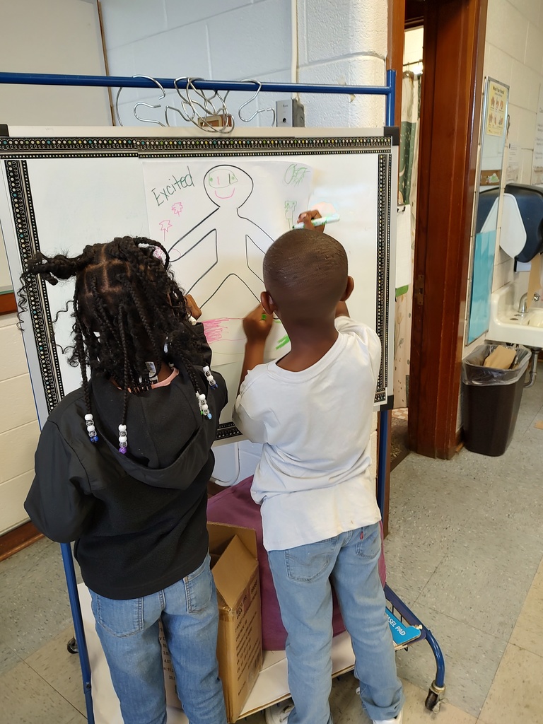 Two students draw on a figure labeled “Excited,” adding a smiling face, bright eyes, and colorful decorations.