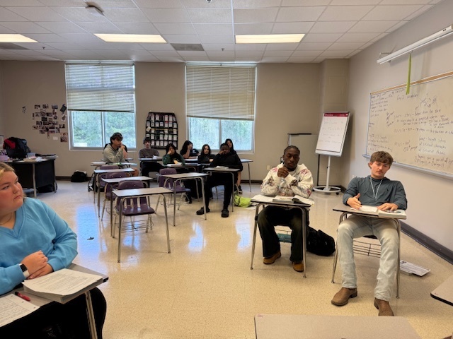 Small groups of students face each other in discussion, acting out roles from The Canterbury Tales trial.