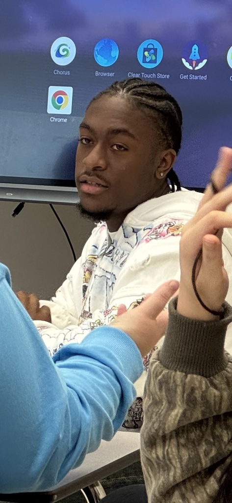 A group of students sit attentively at their desks, listening to classmates present during the mock trial.