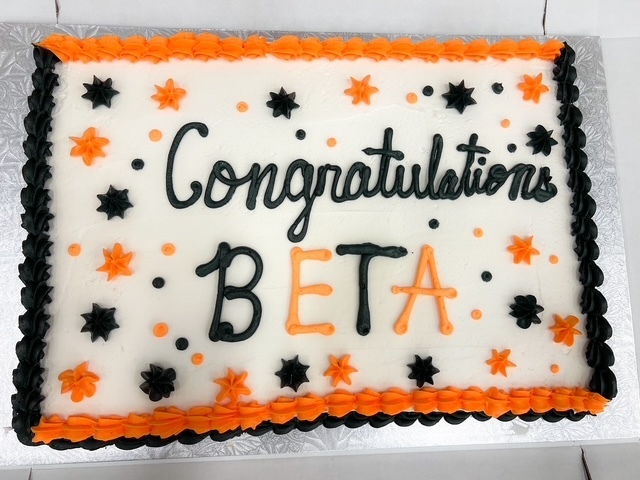 White sheet cake with orange and black trim that says “Congratulations BETA.”