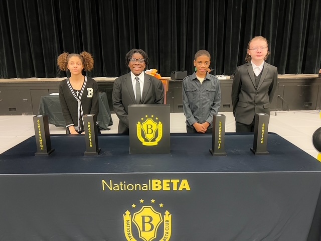 Four students stand behind a National Beta Club table with Beta pillars during the Induction ceremony.