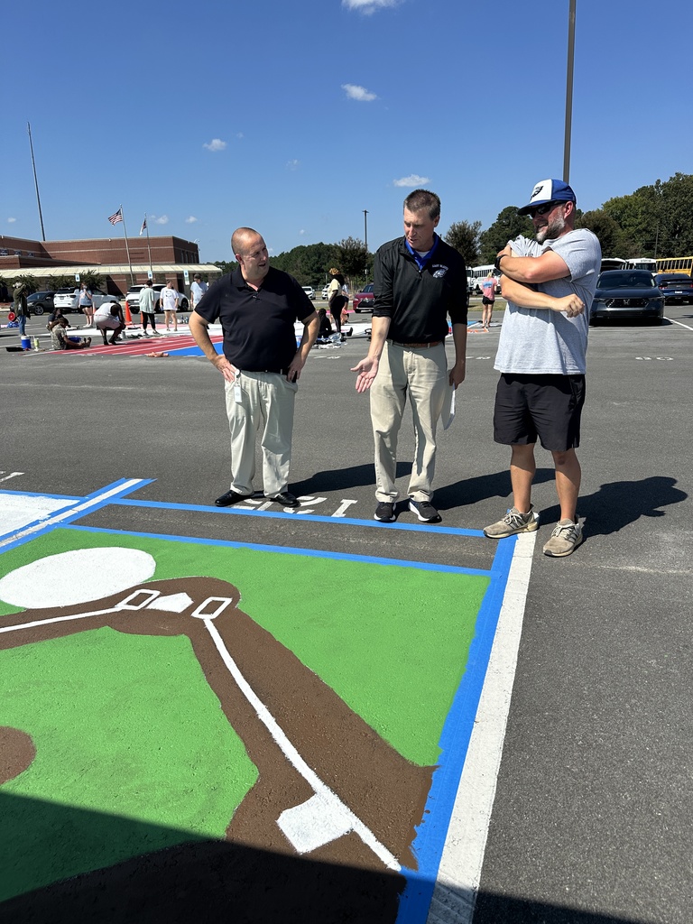 Three adults stand in discussion near a completed baseball field-themed parking spot painted green and brown.