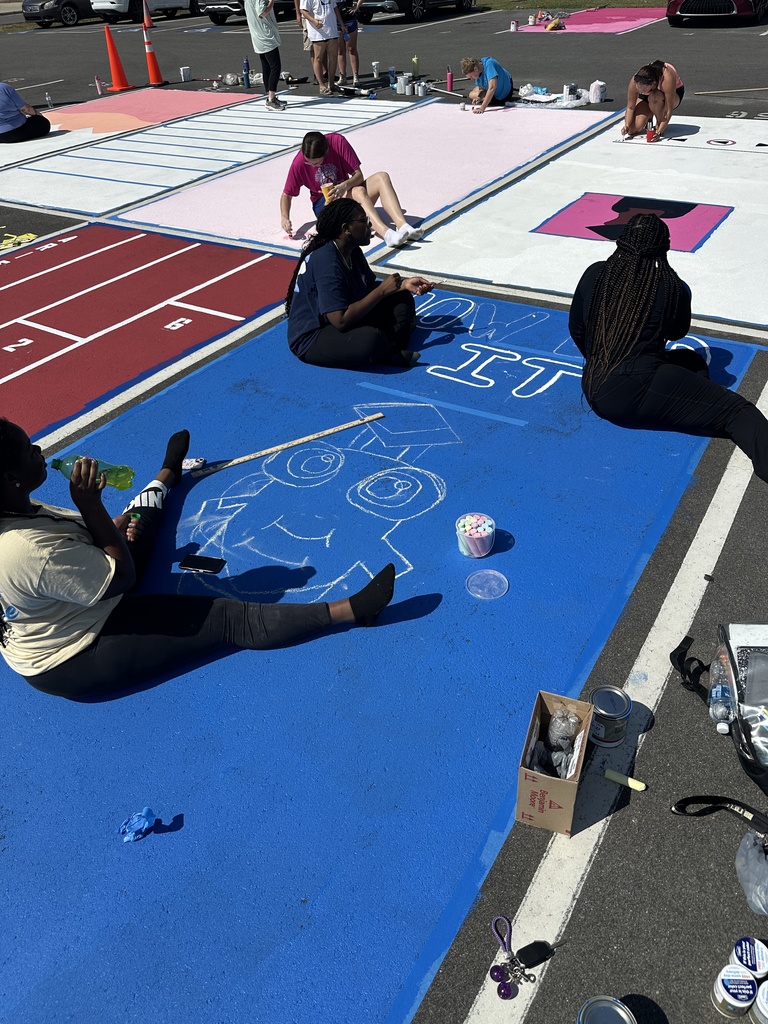Students sit on and around bright blue, pink, and red parking spaces, sketching and painting creative designs.