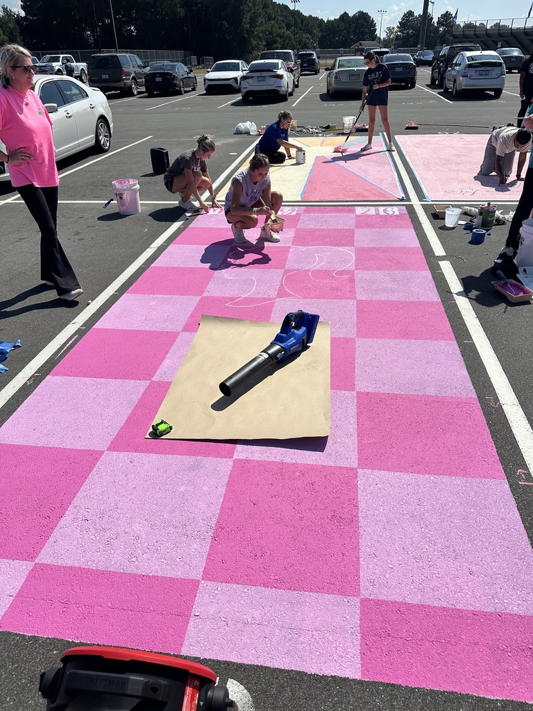 Students work together on pink checkerboard parking space designs, kneeling and sketching with chalk outlines.