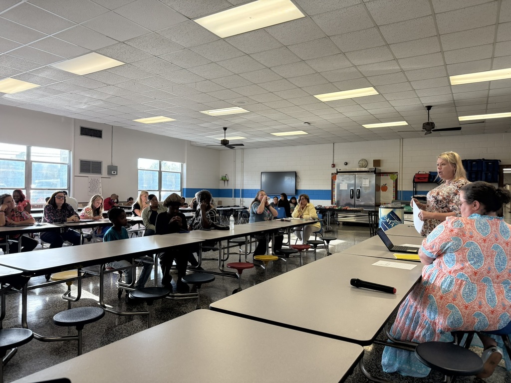 Parents and guardians sit in the cafeteria listening to the principal present information during the first Parent Advisory Meeting of the year.