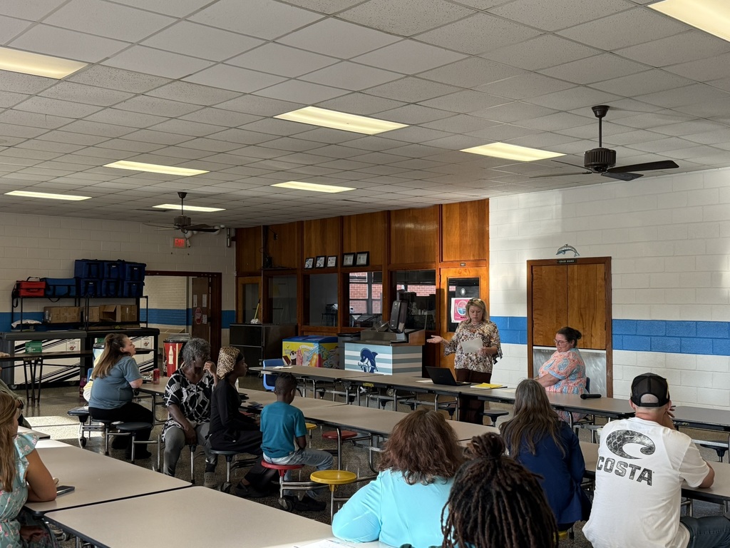 Parents and children listen attentively as two school staff members speak at the front table during the Parent Advisory Meeting.