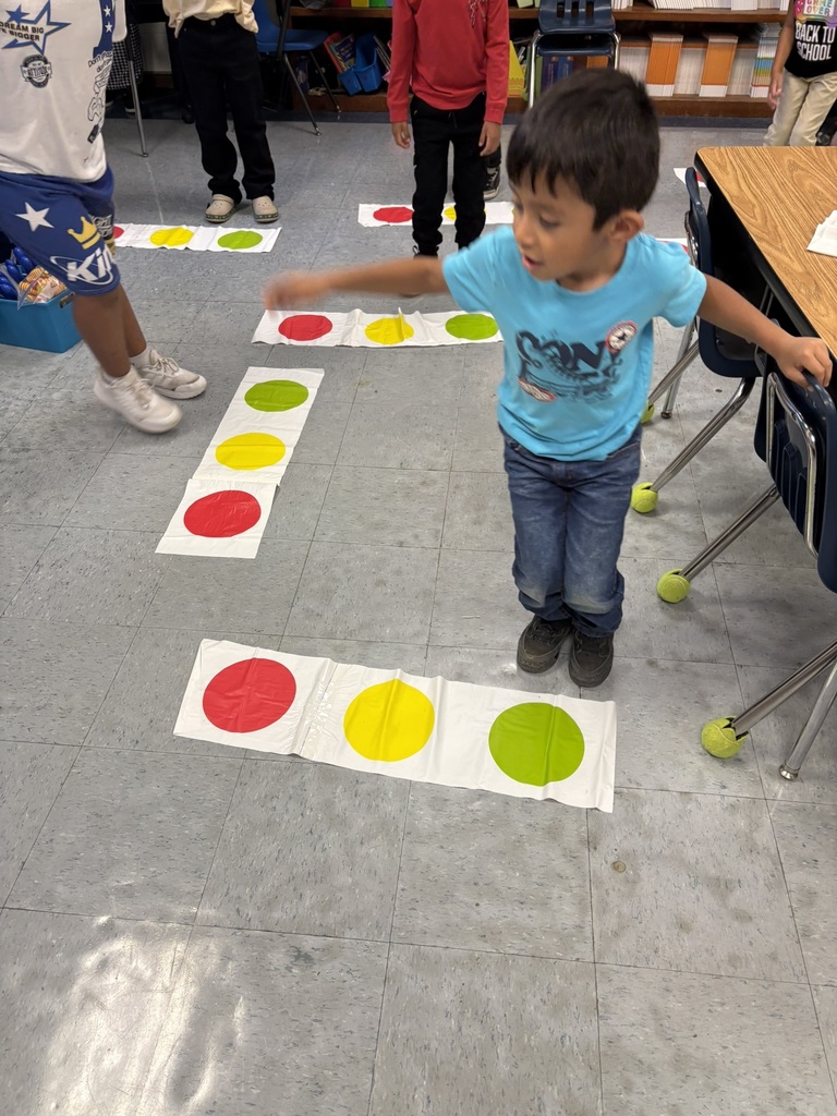 A child in a blue shirt jumps on colored dots while classmates wait their turn.
