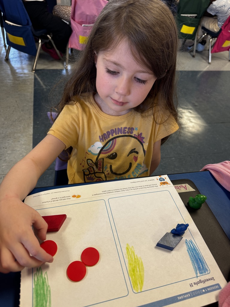 Student in a yellow shirt works carefully with red counters and blue and green math manipulatives on her worksheet.