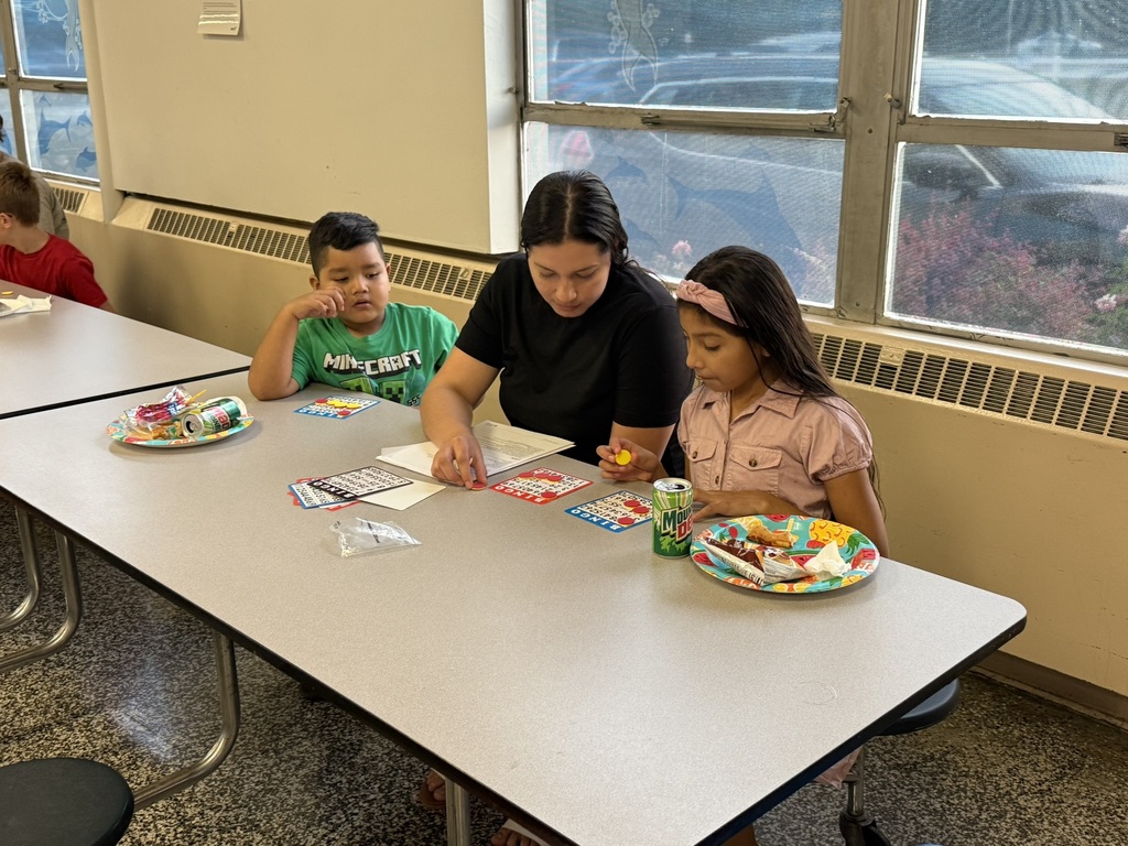 Parent helps two children mark Bingo cards while sharing snacks.