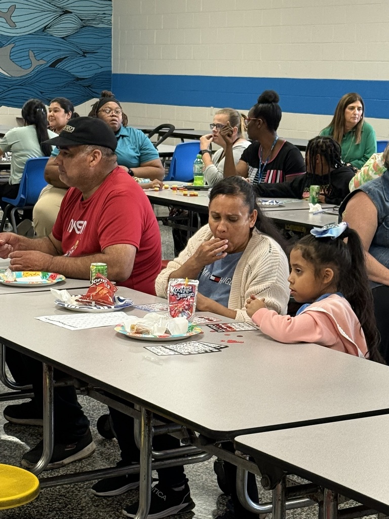 Family enjoys snacks and plays Bingo together at a long cafeteria table.
