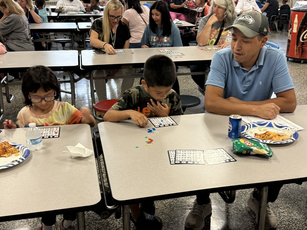 Dad and two children play Bingo at a cafeteria table with food and drinks.