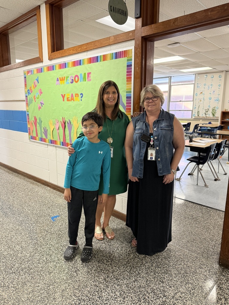 Student and two staff members smile in front of a colorful bulletin board that says “Ready for an awesome year.”