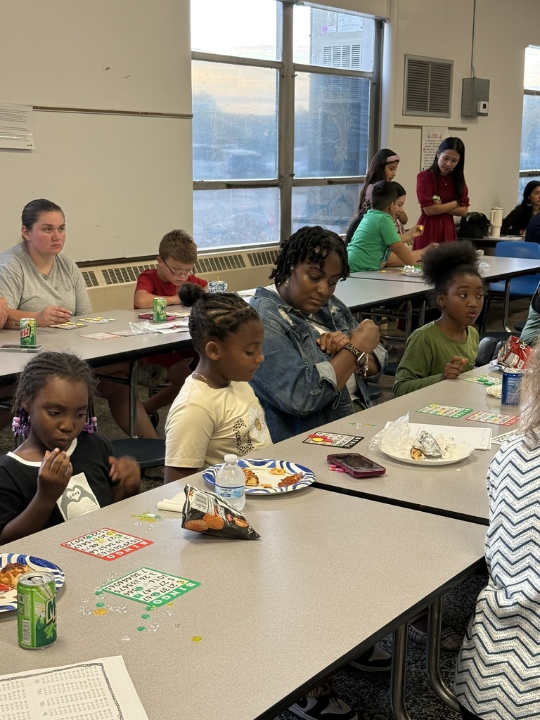 Students and parents sit in rows playing Bingo and enjoying pizza and snacks.