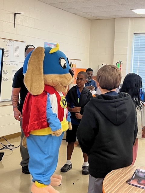 Safety Pup visits a classroom, interacting with students and officers during a safety program.