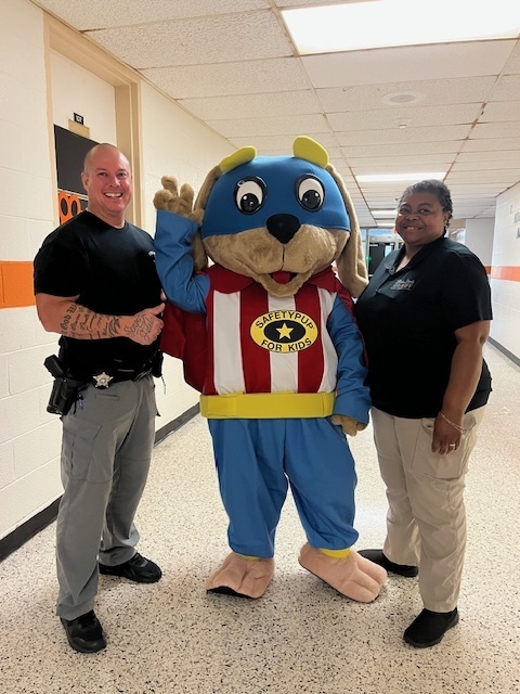 Safety Pup poses with two Bladen County Sheriff’s Department officers in a school hallway, welcoming the program to support kids’ safety.
