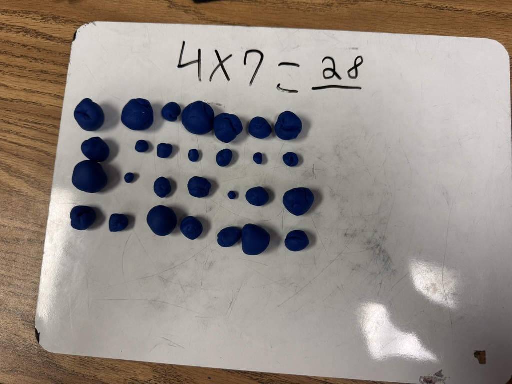 Close-up of a whiteboard with blue Play-Doh pieces arranged in rows under the equation 4 x 7 = 28.