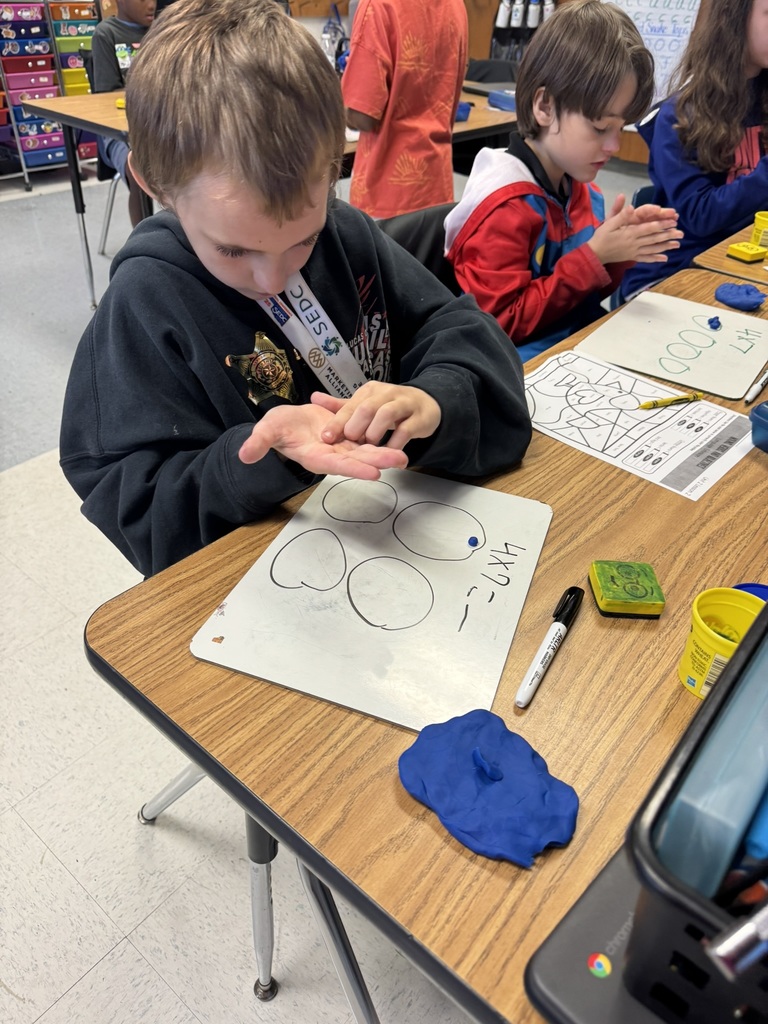 Two students at a round table work with Play-Doh and whiteboards to build multiplication arrays.