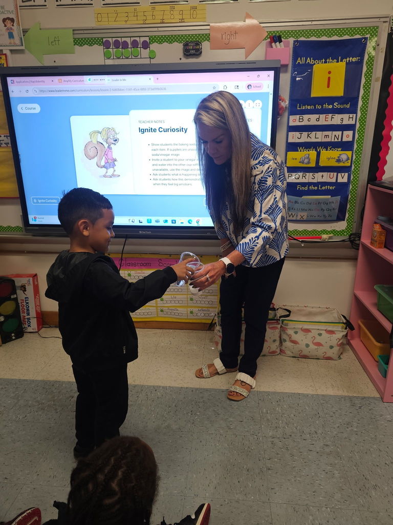 A teacher engages with a young student in a colorful classroom, highlighting a lesson on the screen about igniting curiosity.
