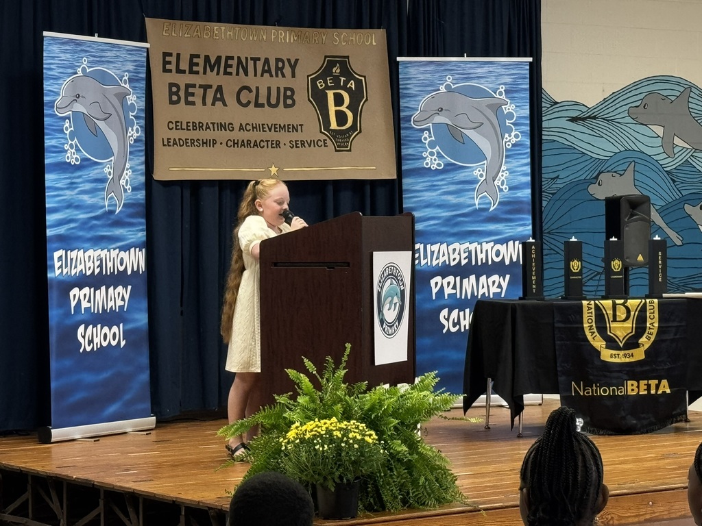 A young speaker stands at a podium during the Elizabethtown Primary School Beta Club ceremony, surrounded by banners and awards.
