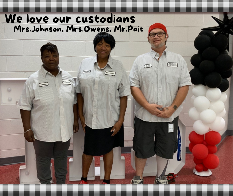 Three school custodians, Mrs. Johnson, Mrs. Owens, and Mr. Pait, standing together smiling in uniform gray shirts. Behind them is a wall with black, white, and red balloon decorations. The text above reads “We love our custodians – Mrs. Johnson, Mrs. Owens, Mr. Pait.”