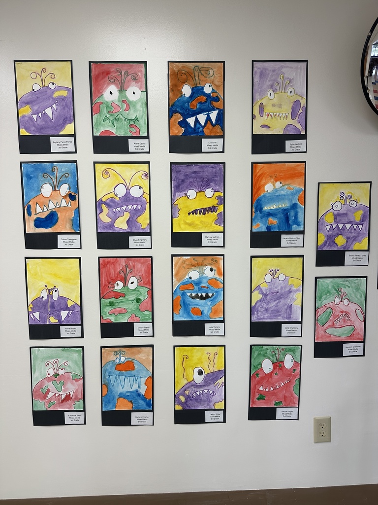 A wall display of 3rd-grade student monster paintings from Bladenboro Primary. Each monster is brightly colored in watercolor, with big eyes, sharp teeth, and creative details like spots, swirls, or antennae, giving each piece a playful and imaginative personality.
