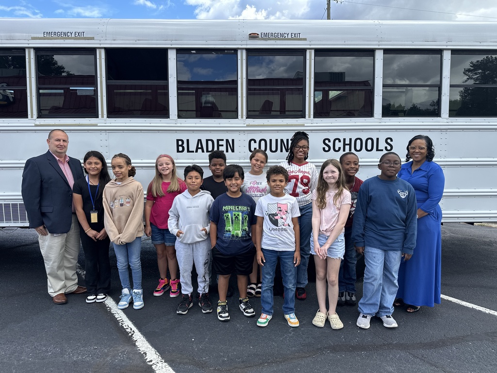 Superintendent Dr. Jason Atkinson and Deputy Superintendent Ann Brown stand with members of the Bladen County Schools Elementary Student Advisory Council in front of a white school bus labeled “Bladen County Schools.” The group of students, dressed in casual clothing, smile for the photo on a sunny day.