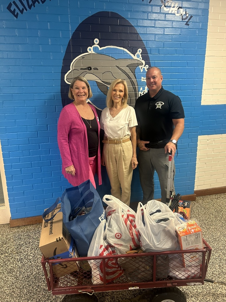 Three people are next to a cart loaded with bags of food, preparing to share the supplies.
