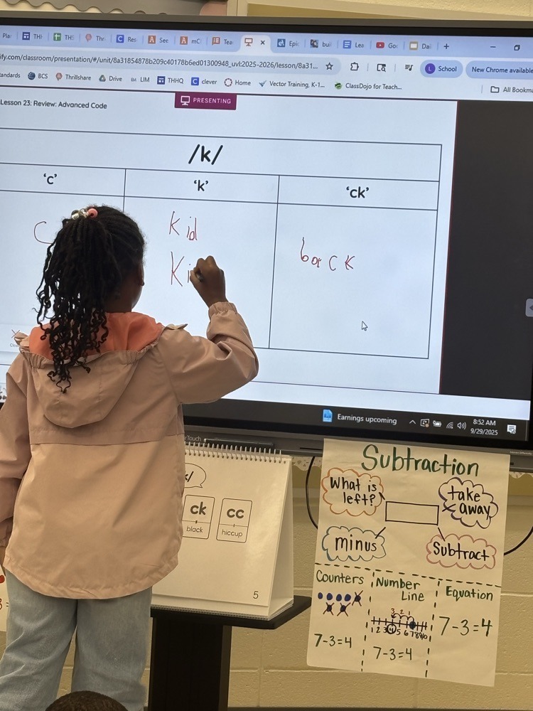 An elementary student writes words on a smartboard during a phonics lesson comparing the sounds for “c,” “k,” and “ck.”