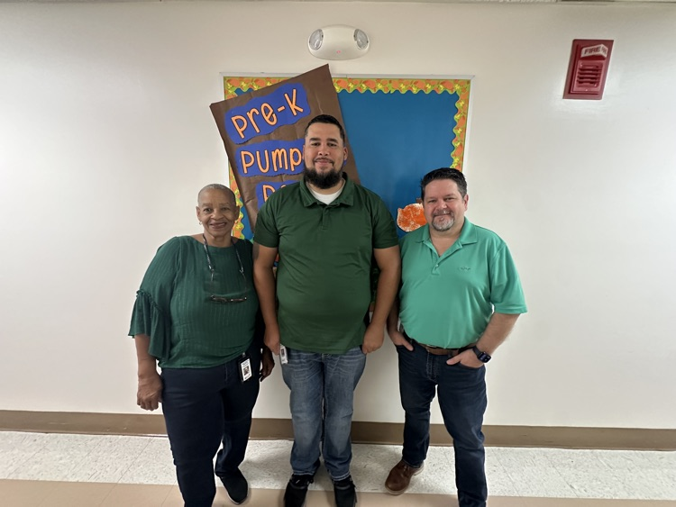 Three Bladen County Schools district office staff members wearing green stand in front of a bulletin board decorated with “Pre-K Pumpkin Patch” letters in recognition of World Mental Health Day.