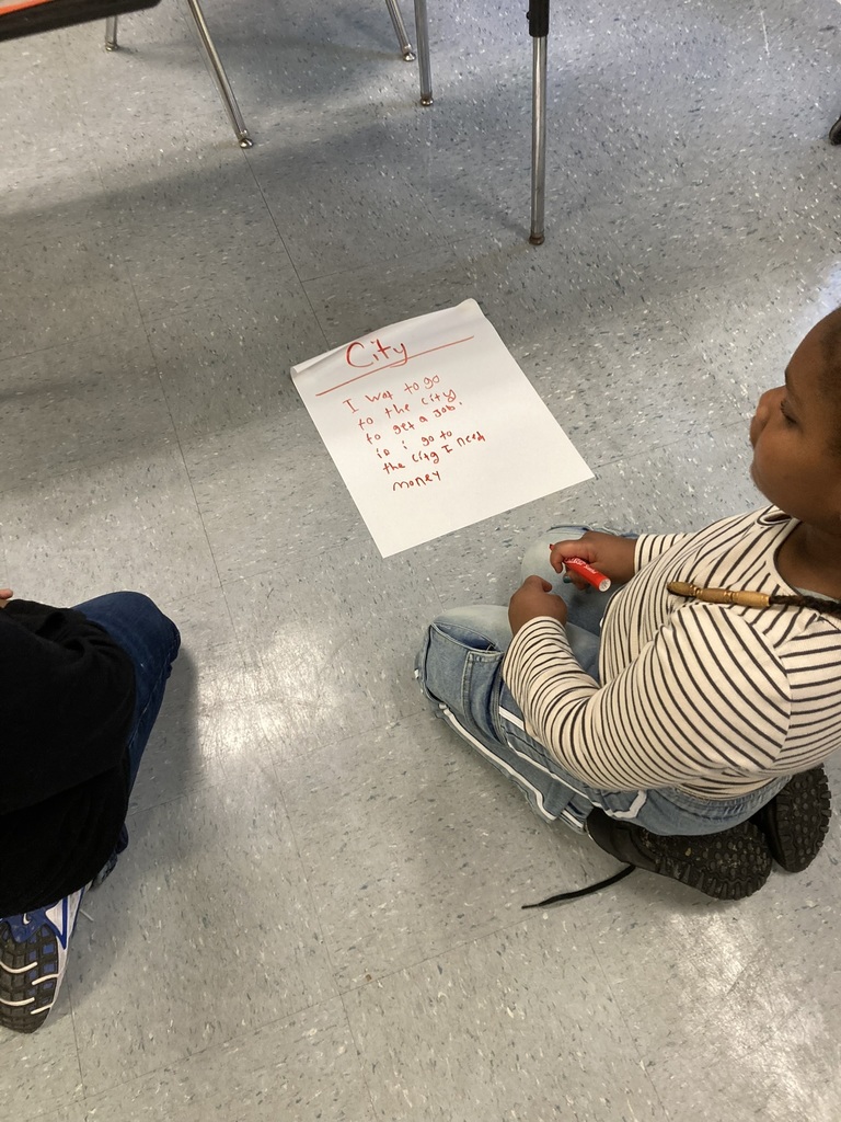 A student sits near a paper labeled “City,” listing reasons to go to the city, such as getting a job and making money.